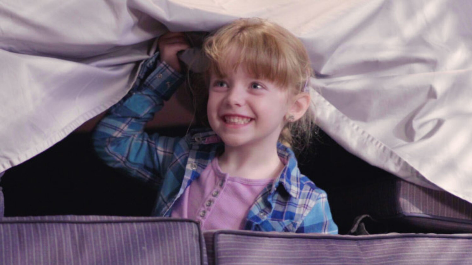 Young Girl smiling while poking her head out of a blanket fort on the set of Are You Ready?
