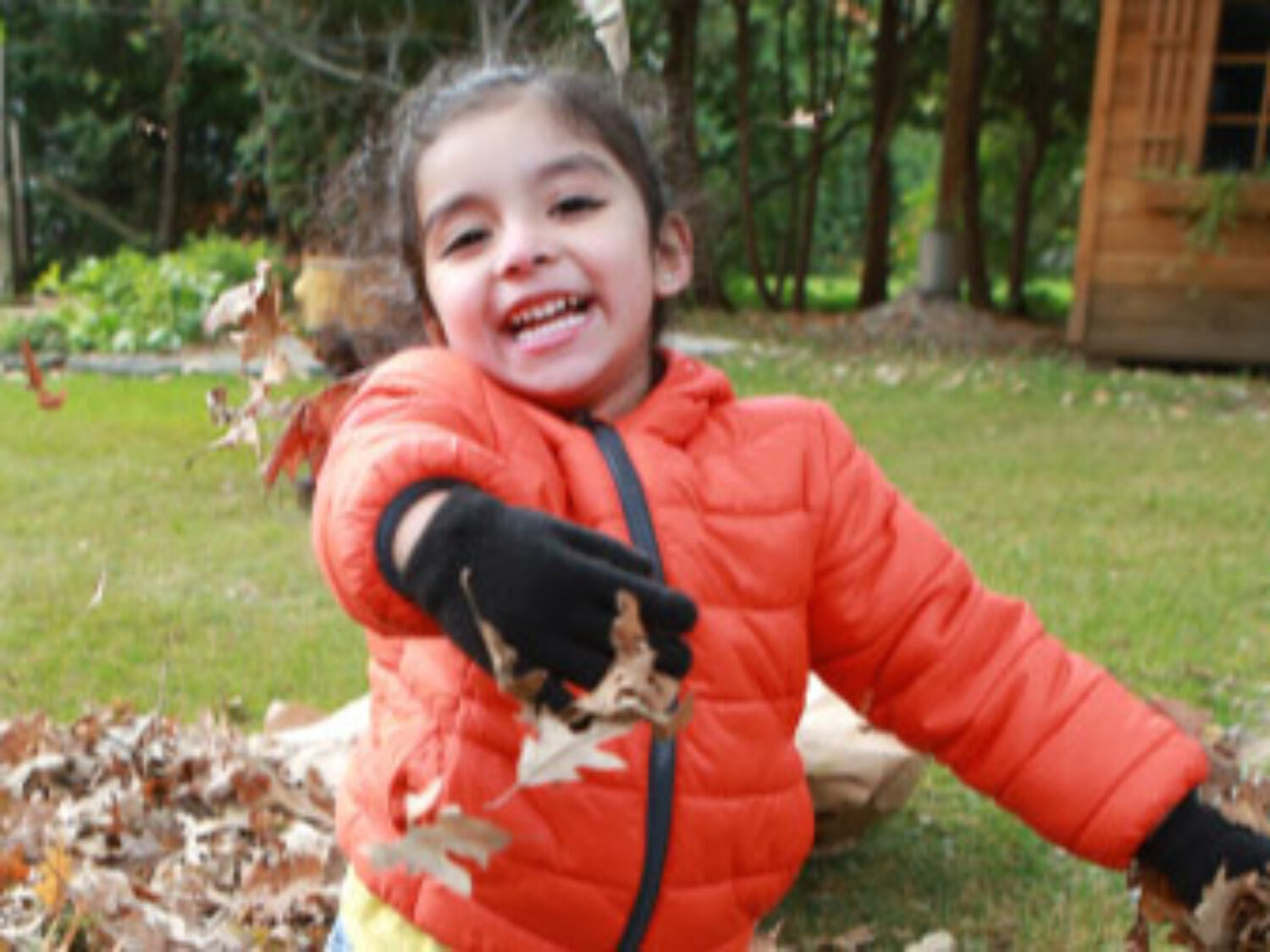 Young girl smiling for the camera while she plays in a pile of leaves