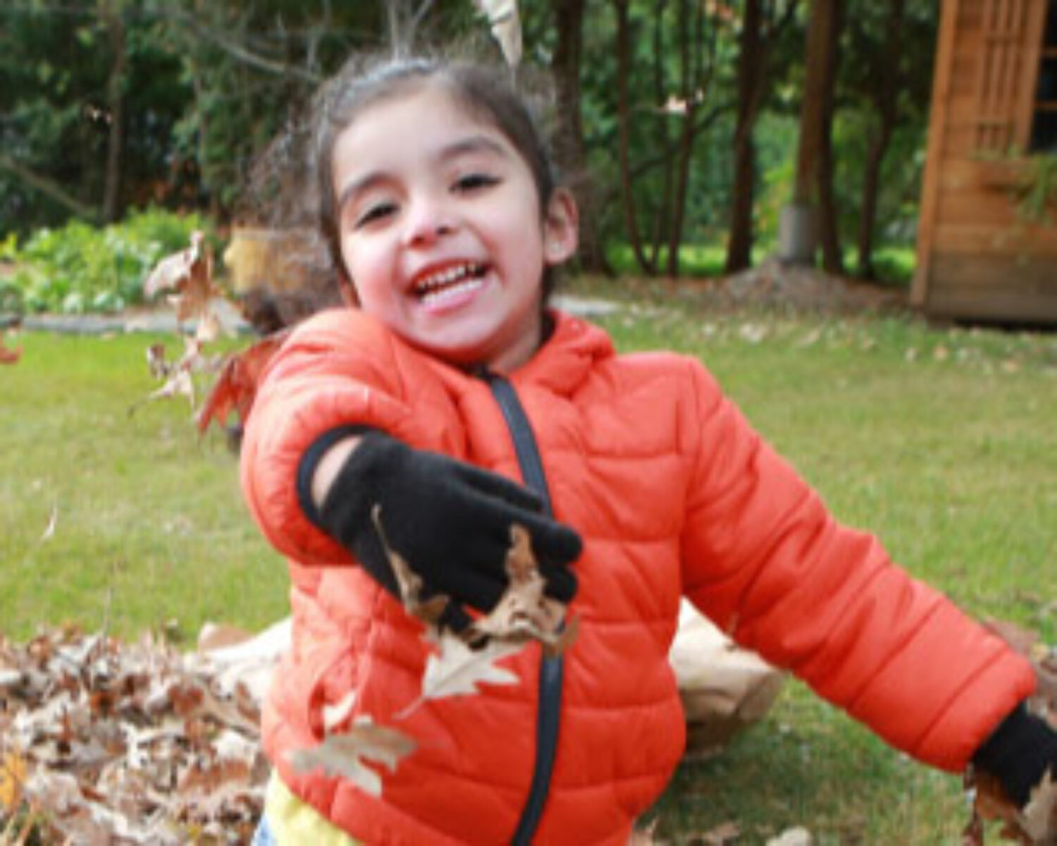 Young girl smiling for the camera while she plays in a pile of leaves