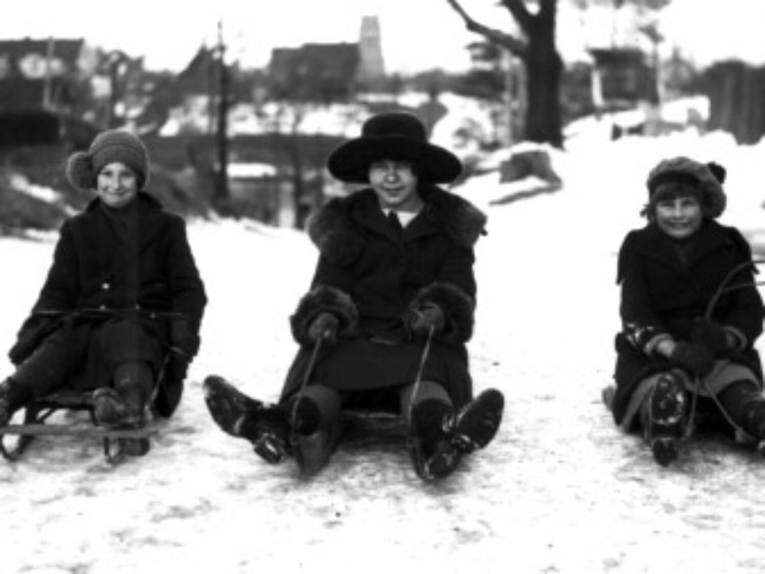 Three women on toboggans in a black and white photo