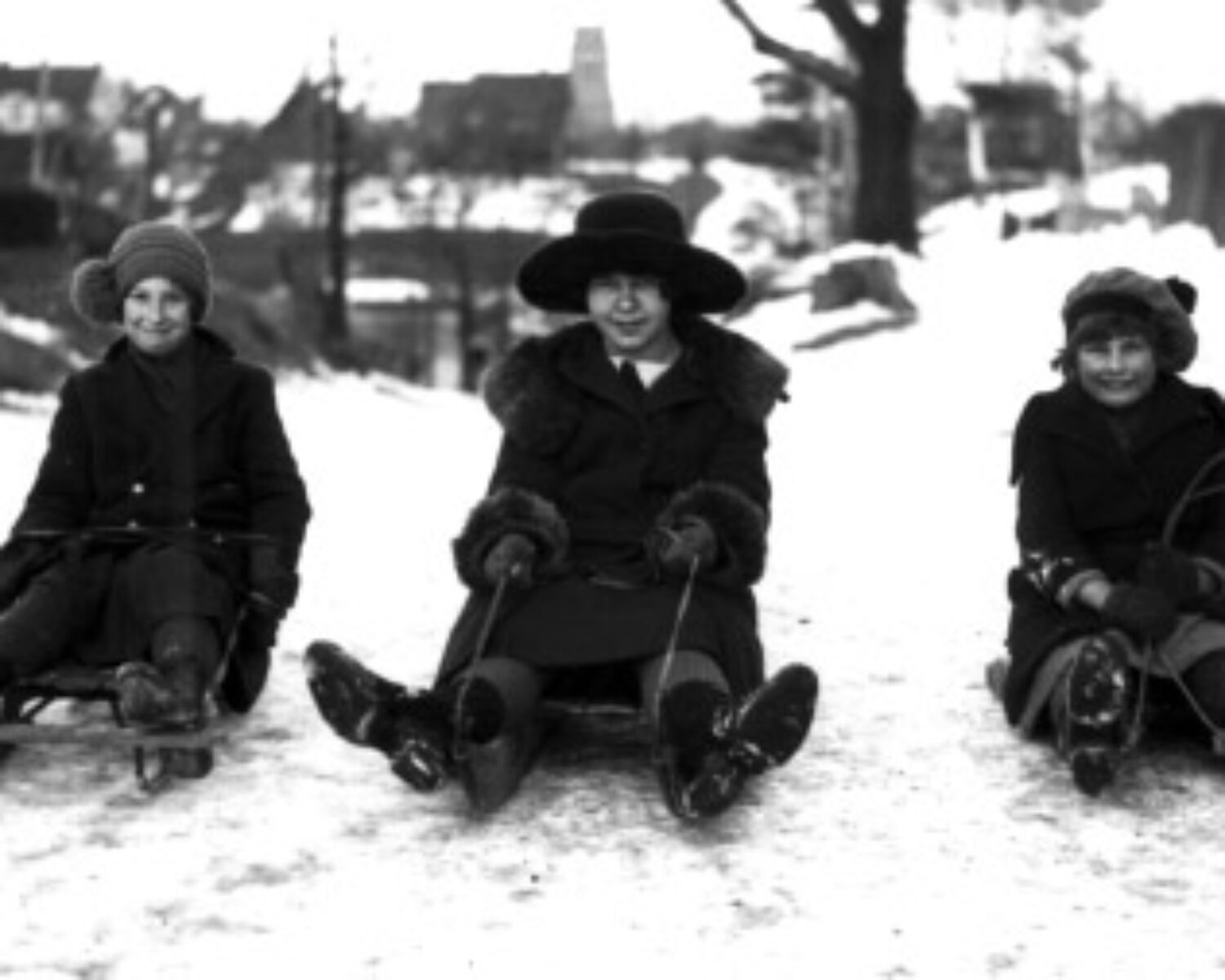 Three women on toboggans in a black and white photo
